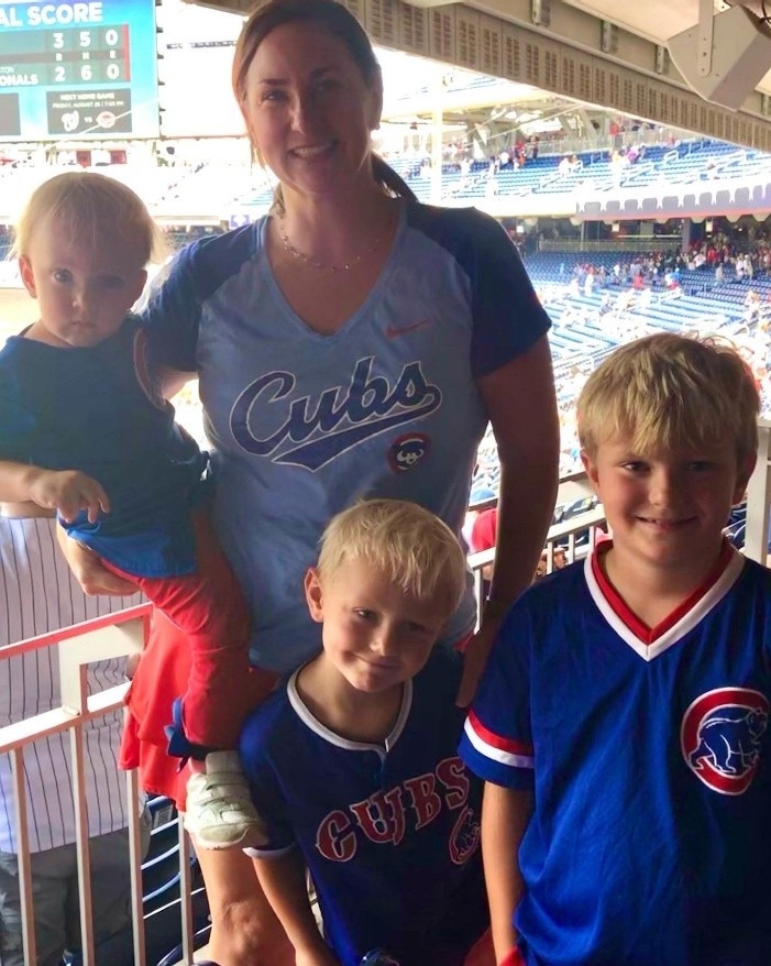 A woman in a Cubs shirt stands with three children, all wearing Cubs gear, while enjoying a baseball game at the stadium.