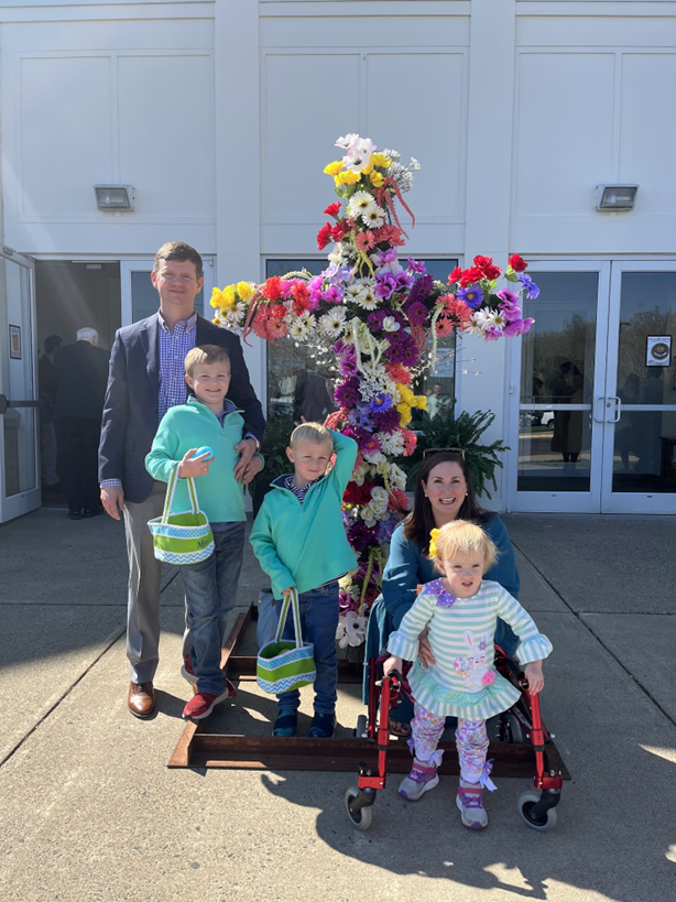 Family posing with a flower-covered cross and Easter baskets.